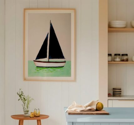 A framed art print of a minimalist sailboat with dark navy blue sails, floating on mint green water against a light beige background. The vertical print is housed in a light wood frame and hangs on a white, vertical-shiplap wall.