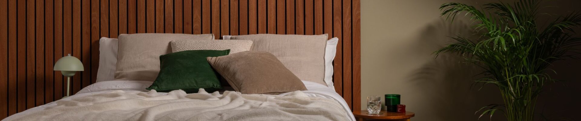 A cosy, modern bedroom featuring a bed with a large, warm-toned Sapele wood slat wall panel serving as a floor-to-ceiling headboard.