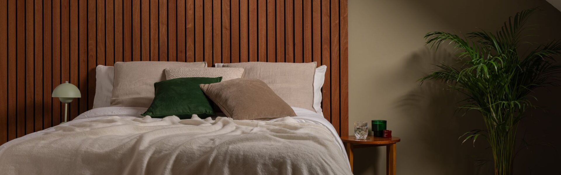 A cosy, modern bedroom featuring a bed with a large, warm-toned Sapele wood slat wall panel serving as a floor-to-ceiling headboard.