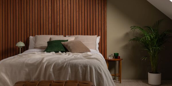 A cosy, modern bedroom featuring a bed with a large, warm-toned Sapele wood slat wall panel serving as a floor-to-ceiling headboard.
