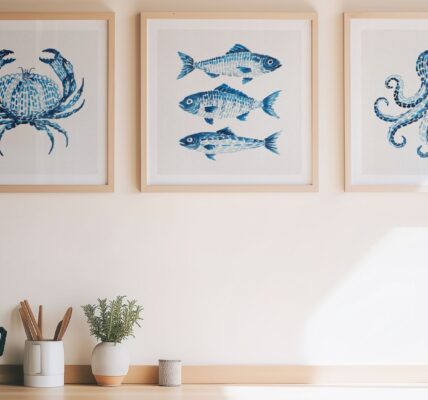 Three square, light-wood framed art pieces hang on a neutral beige wall above a kitchen countertop. Each frame features a watercolor-style illustration in shades of blue against a white background, depicting marine life: a crab on the left, three stacked fish in the center, and an octopus on the right.