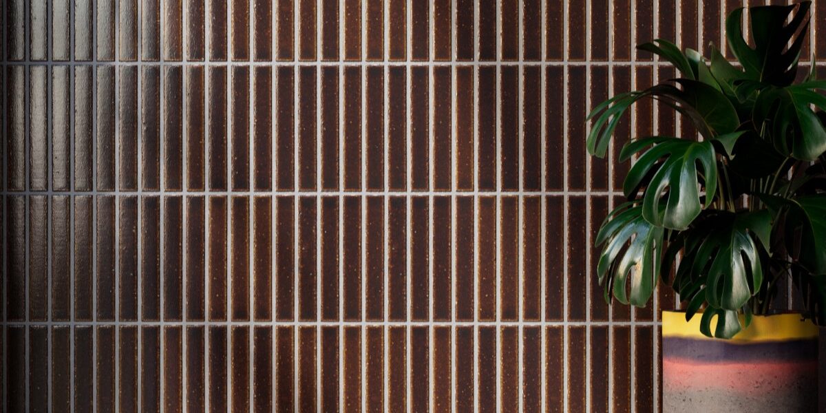 Vertically stacked Kaji Border Japanese porcelain tiles in burnt russet brown with light grout, featured behind a potted Monstera plant.