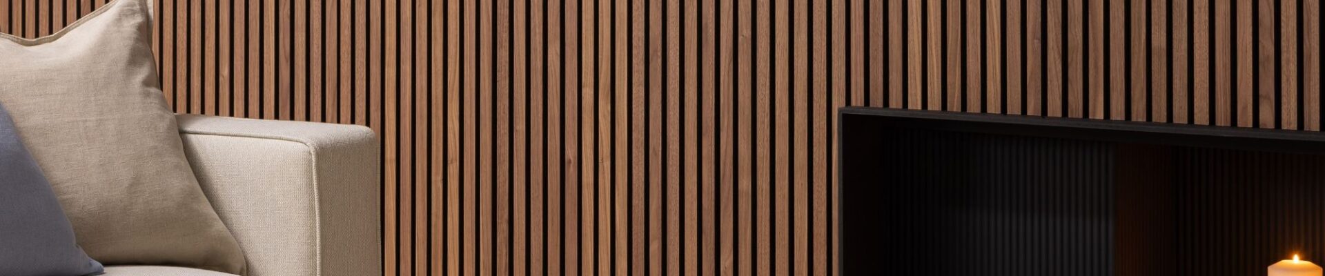 Deep walnut acoustic slatwall panelling mounted on a living room wall behind a sofa and fireplace