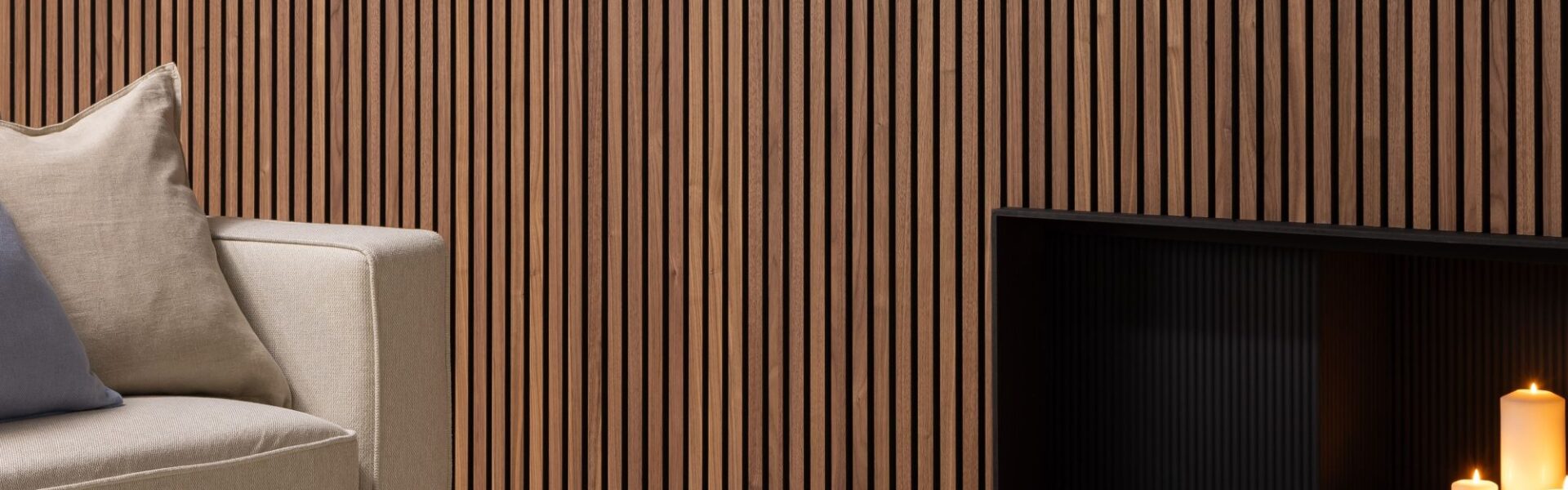 Deep walnut acoustic slatwall panelling mounted on a living room wall behind a sofa and fireplace