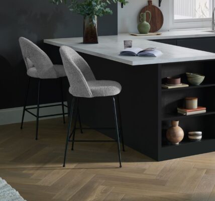 Modern kitchen featuring light oak herringbone engineered wood flooring, a black kitchen island with white marble countertop, and grey bouclé bar stools.