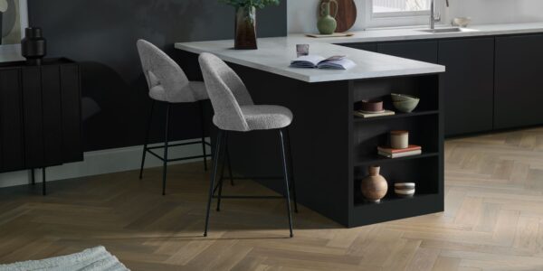 Modern kitchen featuring light oak herringbone engineered wood flooring, a black kitchen island with white marble countertop, and grey bouclé bar stools.