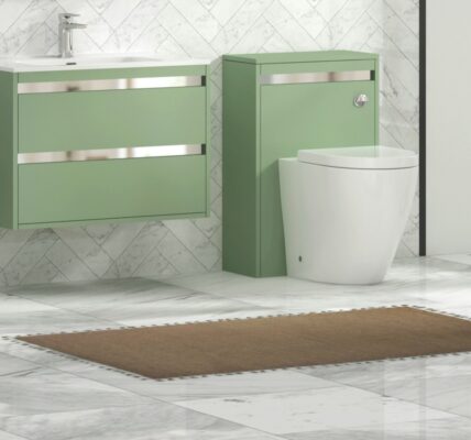 Modern bathroom featuring a wall-hung mint/sage green vanity unit with a white ceramic basin and chrome trim, paired with a matching back-to-wall toilet unit. The space is finished with white marble tiled walls in a herringbone pattern, light marble floor tiles, a brown bath mat, and decorative greenery in a clear vase.