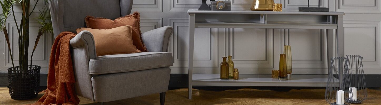 Natural oak herringbone engineered wood flooring in a styled living room setting with a grey armchair and console table