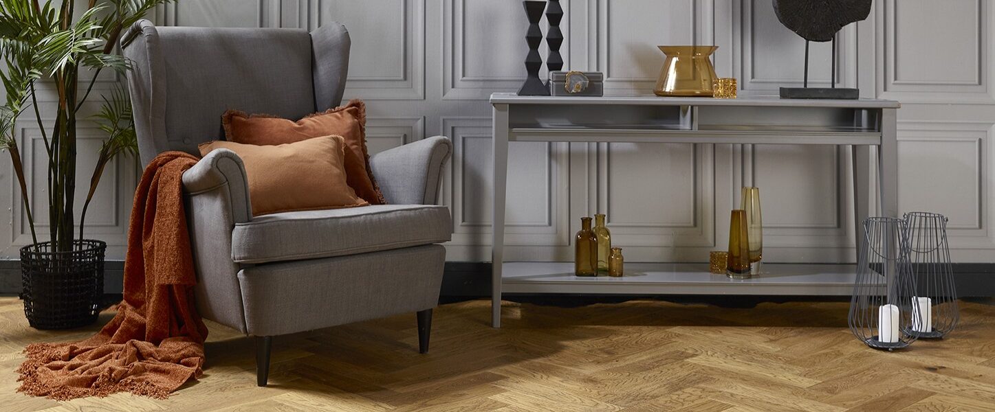 Natural oak herringbone engineered wood flooring in a styled living room setting with a grey armchair and console table