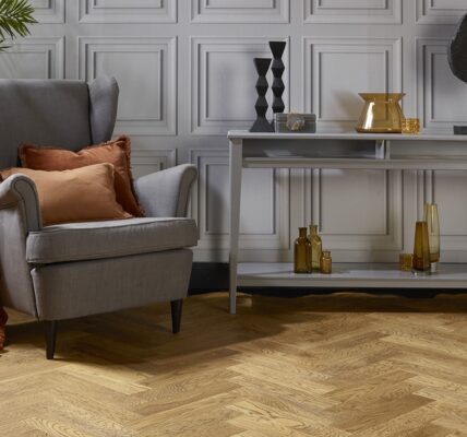 Natural oak herringbone engineered wood flooring in a styled living room setting with a grey armchair and console table