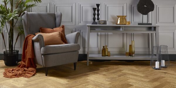 Natural oak herringbone engineered wood flooring in a styled living room setting with a grey armchair and console table