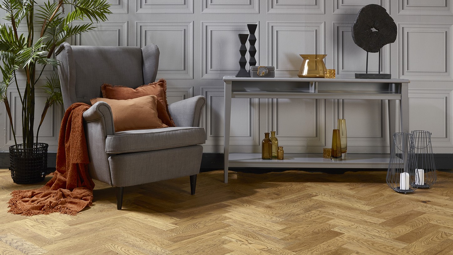 Natural oak herringbone engineered wood flooring in a styled living room setting with a grey armchair and console table