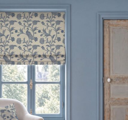 Escape to the Chateau L'Oiseau du Chateau Roman blind in blue featuring a vintage botanical bird and floral pattern, hung over a window in a blue room with a distressed wooden door