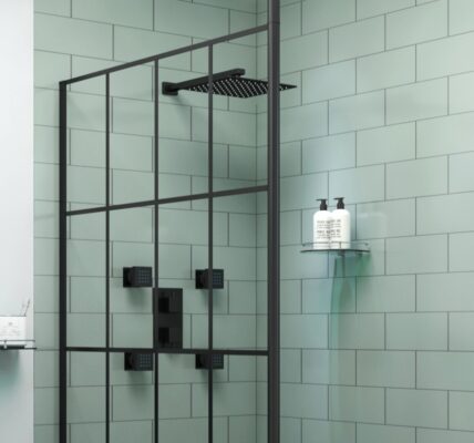 A modern bathroom featuring a black grid wet room shower screen against sage green subway tiles, alongside a black rainfall shower head and matching fixtures.